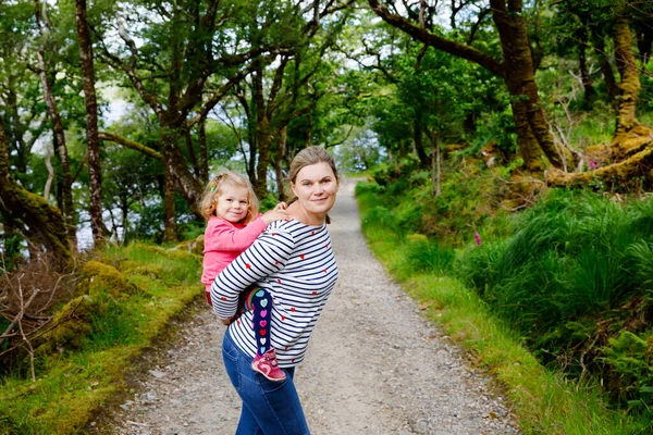 Mãe segurando pequena menina no parque nacional Glenveagh, na Irlanda. Sorrindo e rindo bebê criança e mulher se divertindo passando férias em família na natureza. Viajar com crianças pequenas — Fotografia de Stock