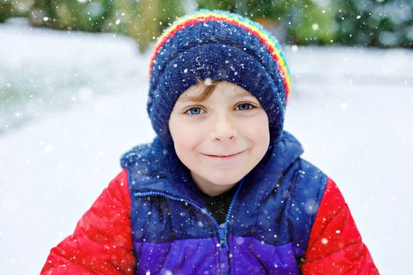 Portrait of little school kid boy in colorful clothes playing outdoors during snowfall. Active leisure with children in winter on cold snowy days. Happy healthy child having fun and playing with snow. — Stock Photo, Image
