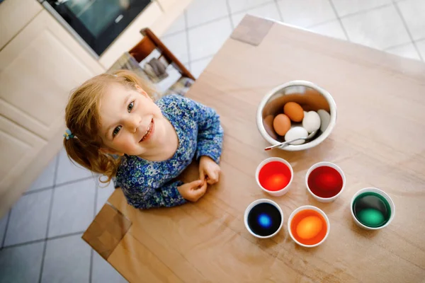 Aufgeregte kleine Mädchen färben Eier für Ostern. Nettes glückliches Kind, das überrascht auf bunte Eier schaut und mit der Familie Urlaub feiert. Von oben — Stockfoto