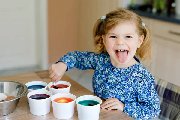 Nadšený batole holka zbarvení vejce na Velikonoce. Roztomilé šťastné dítě, které vypadá překvapeně na barevné vejce, slaví dovolenou s rodinou. Roztomilé dítě doma s různými světlými barvami. — Stock fotografie