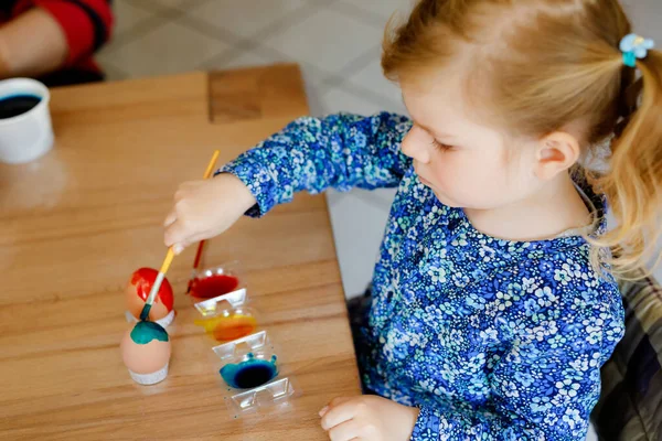 Emocionada niña para colorear huevos para Pascua. Lindo niño feliz buscando sorprendido en coloridos huevos de colores, celebrando la fiesta con la familia. Niño adorable en casa con diferentes colores brillantes. — Foto de Stock