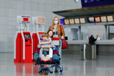Havaalanında maskeli iki küçük çocuk, kız, erkek ve anne. Çocuklar, aile Corona virüsü salgını sırasında uçakla seyahat eder. Önleyici tedbir olarak maskeli insanlar ve kabarık koruma
