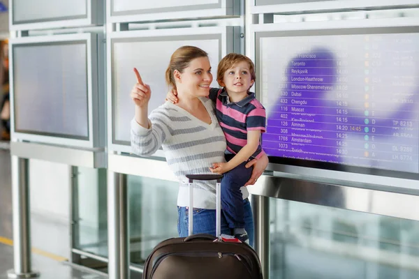 Ung mor som håller i småbarn, gulligt barn på flygplatsen. Liten pojke och mamma, familj reser tillsammans, åker på semester via flygplan och checkar in på elektroniska ombord terminalen. Familjeresor — Stockfoto