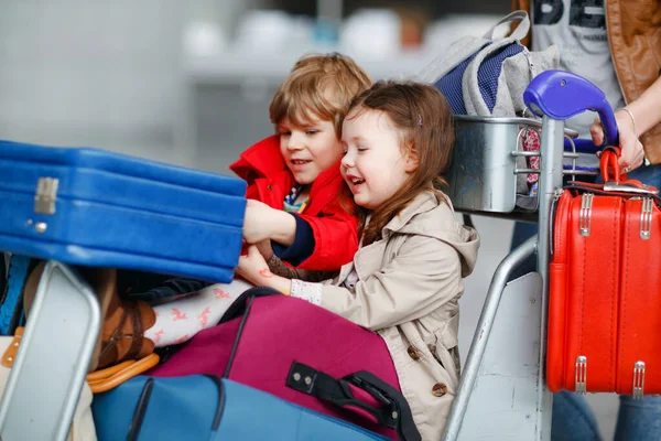 Zwei kleine Kinder, Junge und Mädchen, Geschwister und Mutter am Flughafen. Kinder, Familie auf Reisen, Urlaub mit dem Flugzeug und Warten auf Trolley mit Koffern, die von Frau am Terminal auf Flug geschoben werden. — Stockfoto