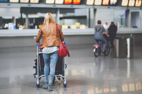 Female travel tourist pushing trolley with luggage at airport terminal. Unrecognizable faceless woman going to airline check in or boarding and waiting for her plane. Travel lifestyle.