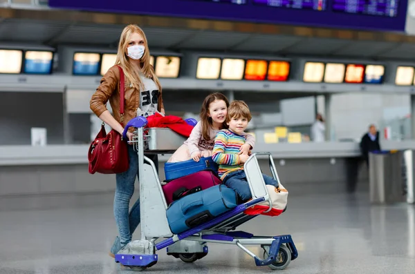 Due bambini piccoli, maschio e femmina e madre in maschera medica all'aeroporto. Bambini, la famiglia viaggia in aereo durante il blocco pandemico del virus della corona. Persone mascherate come misura preventiva e protezione dei merluzzi — Foto Stock