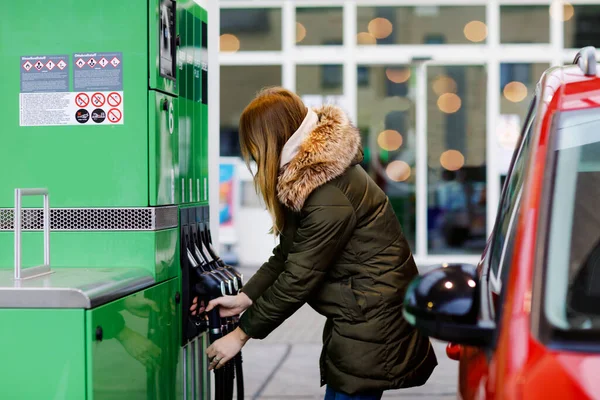 Les femmes portent un masque médical à la station-service libre-service, retiennent la buse de carburant, ravitaillent la voiture en essence pendant le confinement en cas de pandémie du virus corona. Les personnes masquées comme mesure préventive et protection contre la coagulation — Photo