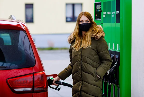 Las mujeres usan máscara médica en la gasolinera de autoservicio, sostienen la boquilla de combustible, repostan el auto con gasolina durante el bloqueo pandémico del virus corona. Las personas con máscaras como medida preventiva y protección covid — Foto de Stock