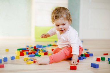 Eğitici oyuncaklarla oynayan tatlı küçük bir kız. Mutlu sağlıklı çocuk evde ya da çocuk odasında renkli tahta bloklarla eğleniyor. Bebek sürünüyor, renkleri ve biçimleri öğreniyor.