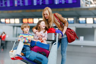 İki küçük çocuk, erkek ve kız, kardeşler ve anne havaalanında. Çocuklar, aile seyahati, uçakla tatile gitmek ve bir kadının terminalden uçmak için ittiği valizlerle tramvayda beklemek..