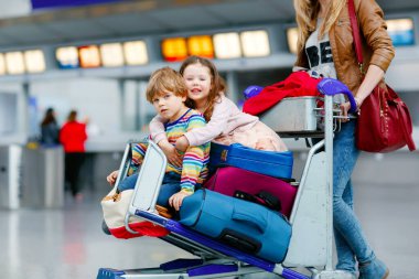 İki küçük çocuk, erkek ve kız, kardeşler ve anne havaalanında. Çocuklar, aile seyahati, uçakla tatile gitmek ve bir kadının terminalden uçmak için ittiği valizlerle tramvayda beklemek..