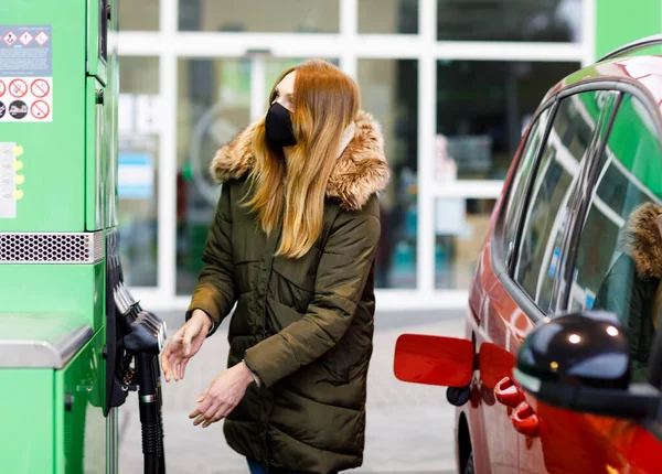 Las mujeres usan máscara médica en la gasolinera de autoservicio, sostienen la boquilla de combustible, repostan el auto con gasolina durante el bloqueo pandémico del virus corona. Las personas con máscaras como medida preventiva y protección covid — Foto de Stock