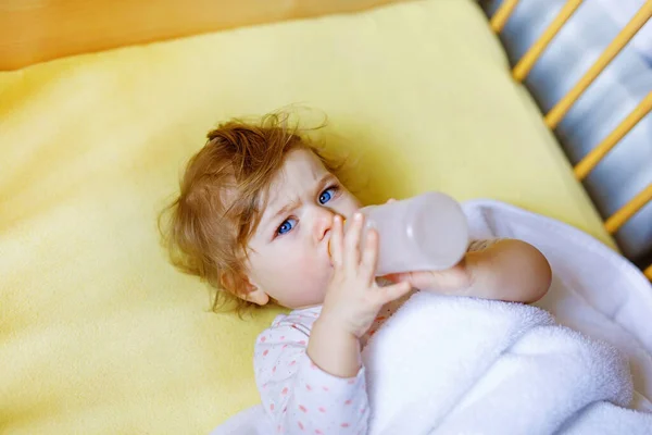 Menina bonito segurando mamadeira com fórmula suave e beber. Criança em cama de berço antes de dormir — Fotografia de Stock