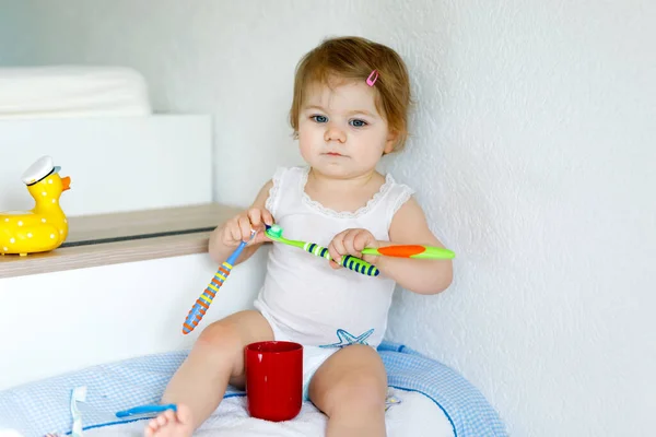 Маленькая девочка держит зубную щетку и чистит первые зубы. Малыш учится чистить молочный зуб. Концепция профилактики, гигиены и здравоохранения. Счастливый ребенок в ванной комнате — стоковое фото