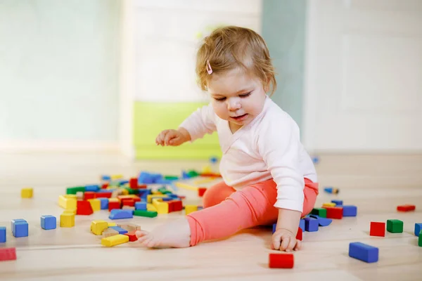 Bonito menina brincando com brinquedos educativos. Criança saudável feliz se divertindo com blocos de madeira diferentes coloridos em casa ou no berçário. Criança rastejando e aprendendo cores e formas, dentro de casa — Fotografia de Stock