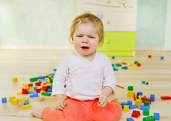 Zaklatott síró kislány oktatási játékokkal. Szomorú fáradt vagy éhes egyedül egészséges gyermek ül közelében színes különböző fatömbök otthon vagy óvoda. Eltűnt anya a bölcsiben. — Stock Fotó