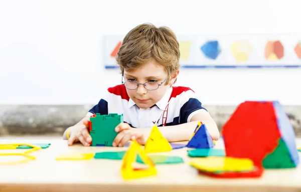 Ευτυχισμένο παιδί αγόρι με γυαλιά που διασκεδάζει με την οικοδόμηση και τη δημιουργία γεωμετρικών μορφών, μαθαίνοντας μαθηματικά και γεωμετρία — Φωτογραφία Αρχείου