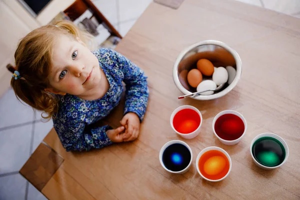 Возбужденная маленькая девочка раскрашивает яйца на Пасху. Симпатичный счастливый ребенок, удивленный красочными цветными яйцами, празднует праздник с семьей. Сверху неопознанное лицо. — стоковое фото