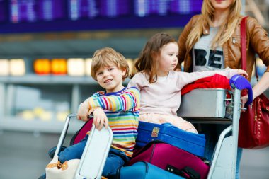 İki küçük çocuk, erkek ve kız, kardeşler ve anne havaalanında. Çocuklar, aile seyahati, uçakla tatile gitmek ve bir kadının terminalden uçmak için ittiği valizlerle tramvayda beklemek..