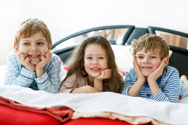 Három boldog gyerek pizsamában ünnepli a pizsamapartit. Óvodás és iskolás fiúk és lányok jól érzik magukat együtt. — Stock Fotó