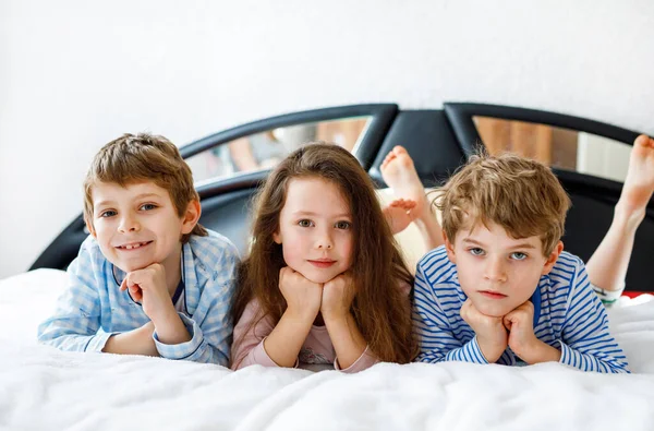 Pijamalı üç mutlu çocuk pijama partisini kutluyor. Anaokulu ve okul çocukları ve kız birlikte eğleniyorlar. — Stok fotoğraf