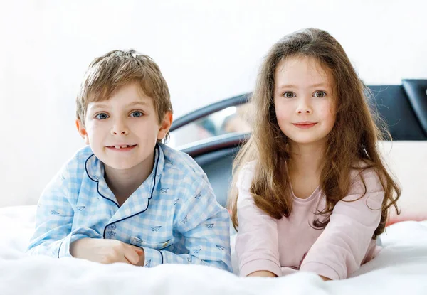 Doi copii fericiţi în pijamale sărbătorind petrecerea pijamalei. Preșcolar și școală băiat și fată se distrează împreună . — Fotografie, imagine de stoc