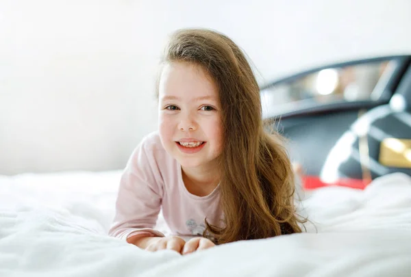 可爱的小女孩，穿着五颜六色的睡衣睡在他的白色旅馆床上，长毛. — 图库照片