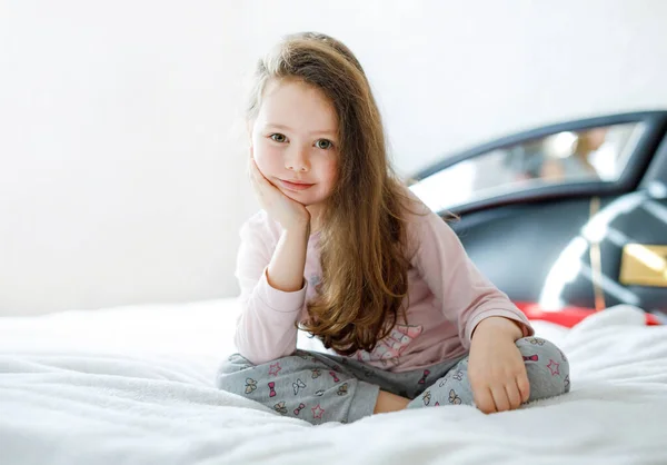 可爱的小女孩，穿着五颜六色的睡衣睡在他的白色床上后，快乐极了. — 图库照片