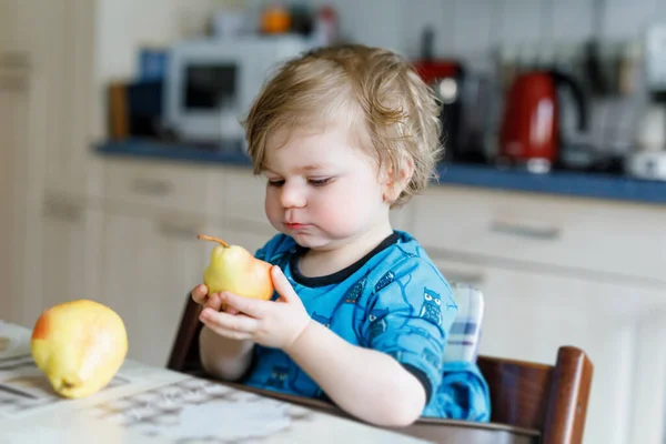 Roztomilé roztomilé batole dívka jíst čerstvé hrušky. Hladové, šťastné dítě jednoho roku držící ovoce. — Stock fotografie