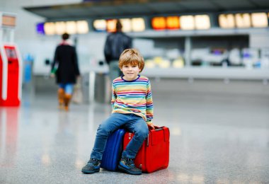 Uluslararası havaalanındaki terminalde büyük bavulları olan küçük mutlu çocuk. Okul öncesi heyecanlı çocuk uçuşu ve tatile çıkmayı bekliyor. Seyahat aile hayatı..
