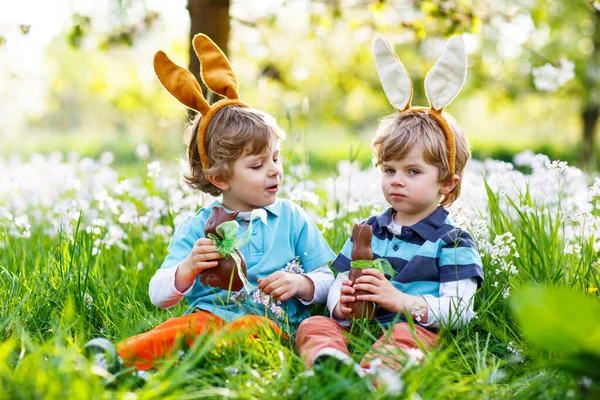 Dos amiguitos en orejas de conejo de Pascua comiendo chocolate — Foto de Stock