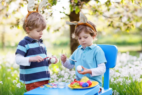 Dos niños pequeños con orejas de conejo de Pascua, pintando huevos de colores —  Fotos de Stock