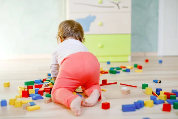 Eğitici oyuncaklarla oynayan tatlı bir kız bebek. Mutlu sağlıklı çocuk evde ya da çocuk odasında renkli tahta bloklarla eğleniyor. Bebek sürünüyor, arkadan bakıyor, yüzü yok, tanınmaz halde. — Stok fotoğraf