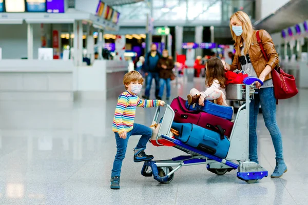 Dwójka małych dzieci, chłopiec, dziewczynka i matka w masce medycznej na lotnisku. Dzieci, rodzina podróżuje samolotem podczas pandemii wirusa korony. Ludzie w masce jako środek zapobiegawczy i ochrony przeciw owadom — Zdjęcie stockowe