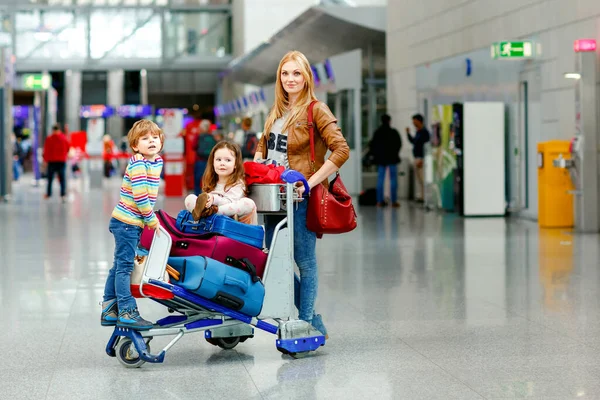 Dos niños pequeños, niño y niña, hermanos y madre en el aeropuerto. Niños, familia viajando, yendo de vacaciones en avión y esperando en el carro con maletas empujando por la mujer en la terminal para el vuelo. — Foto de Stock