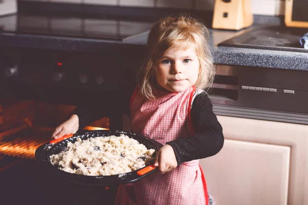 Carina la bambina che cuoce la torta di mele a casa. Felice bambino sorridente che aiuta con torta torta in cucina domestica, in piedi vicino al forno caldo. Cibo sano fatto in casa. — Foto Stock
