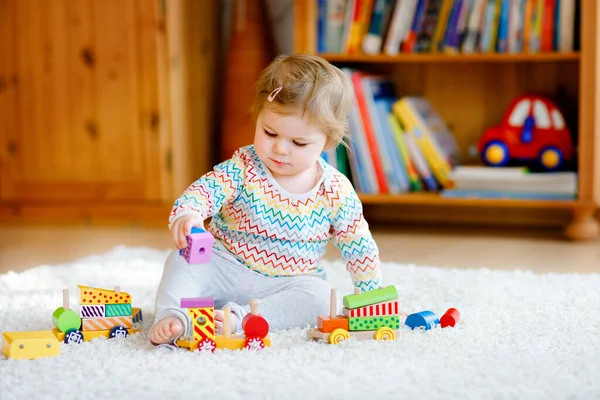 小女孩在家里或托儿所玩教育用的木制玩具。带着五彩缤纷的火车的托德勒孩子们玩不同的玩具。在科罗纳病毒大流行检疫期间孤独的孩子 — 图库照片