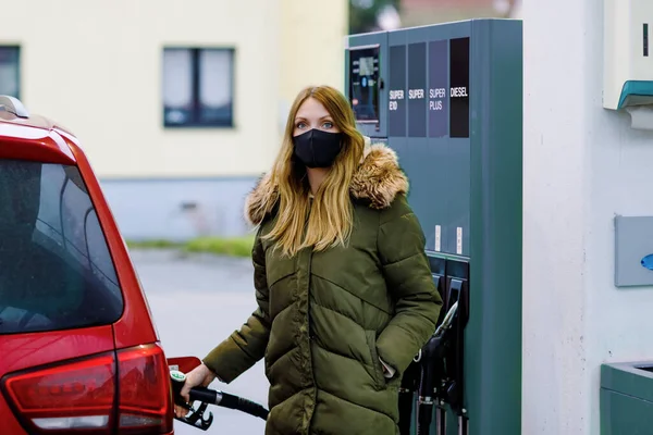 Las mujeres usan máscara médica en la gasolinera de autoservicio, sostienen la boquilla de combustible, repostan el auto con gasolina durante el bloqueo pandémico del virus corona. Las personas con máscaras como medida preventiva y protección covid — Foto de Stock