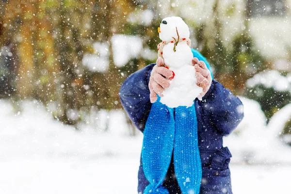 Cute little little maluch girl dokonywania mini bałwana i jedzenia marchewki nosa. Urocze zdrowe, szczęśliwe dziecko bawiące się i bawiące śniegiem, na świeżym powietrzu w chłodny dzień. Aktywny wypoczynek z dziećmi w zimie — Zdjęcie stockowe