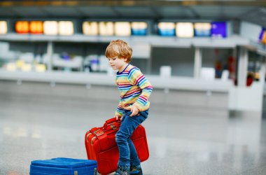 Uluslararası havaalanındaki terminalde büyük bavulları olan küçük mutlu çocuk. Okul öncesi heyecanlı çocuk uçuşu ve tatile çıkmayı bekliyor. Seyahat aile hayatı..