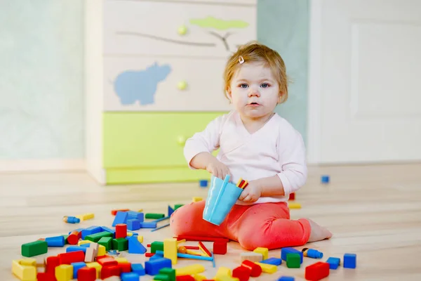 Eğitici oyuncaklarla oynayan tatlı küçük bir kız. Mutlu sağlıklı çocuk evde ya da çocuk odasında renkli tahta bloklarla eğleniyor. Bebek sürünüyor, renkleri ve biçimleri öğreniyor. — Stok fotoğraf