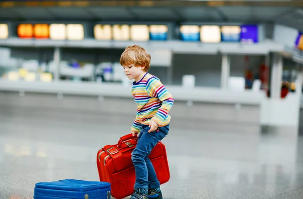 Menino pequeno feliz com bagagem grande mala no terminal no aeroporto internacional. A criança animada pré-escolar espera pelo voo e vai de férias. Viagens estilo de vida familiar. — Fotografia de Stock