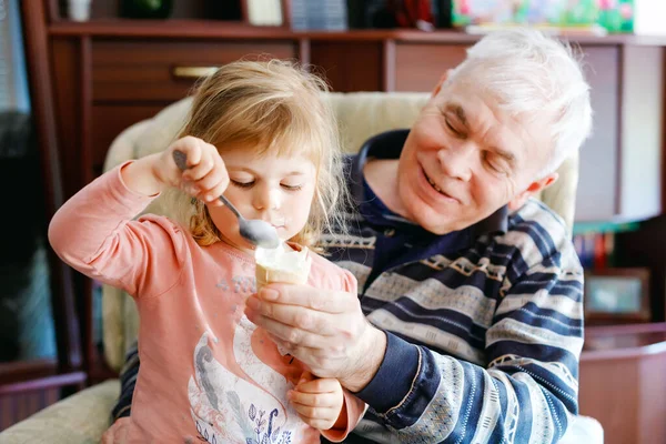 Buon nonno e graziosa nipotina bambino, adorabile bambino mangiare insieme gelato. Famiglia degustazione dolce gelato, neonata alimentazione uomo anziano. — Foto Stock