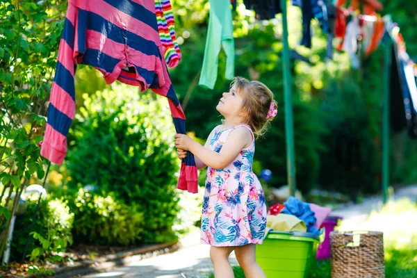 Niña colgando ropa, vestidos limpios frescos y pantalones para secar en el jardín, al aire libre después de hacer la ropa. Feliz niño ayudando en el hogar. Familia trabajando juntos, niño aprendiendo a ayudar. —  Fotos de Stock