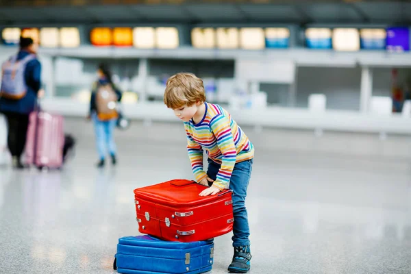 Glücklicher kleiner Junge mit großem Koffer am Terminal des internationalen Flughafens. Aufgeregtes Kind im Vorschulalter wartet auf Flug und Urlaub. Lebensstil der Familie. — Stockfoto