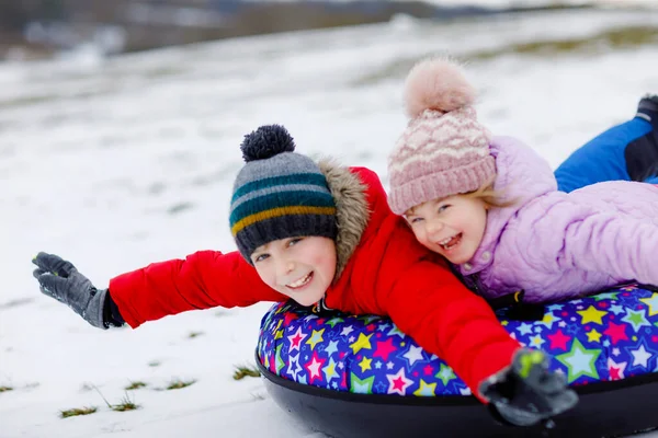 Aktif bir kız ve okul çocuğu kar kanalında birlikte kayıyorlar. Mutlu çocuklar, kardeşler kışın kızakla dışarıda eğleniyorlar. Erkek ve kız kardeş karlı yokuş aşağı tüp, aile zamanı. — Stok fotoğraf