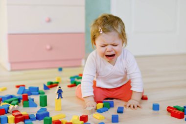 Eğitici oyuncaklarla ağlayan bir kız çocuğu. Üzgün, aç, yalnız, sağlıklı çocuk evde ya da çocuk odasında renkli tahta blokların yanında oturuyor. Bebek kreşte kayıp anne.
