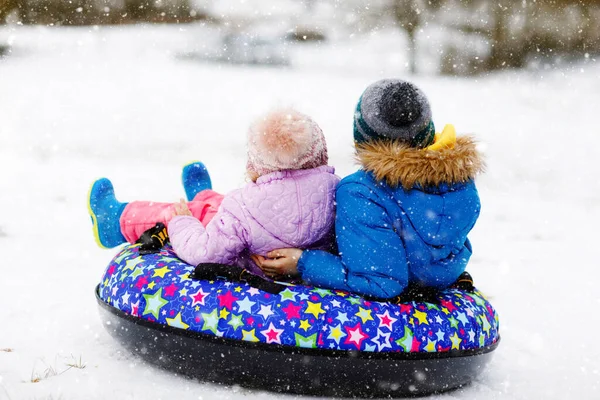 Aktives Kleinkind und Schulkind rutschen gemeinsam auf Schneeröhre den Hügel hinunter. Glückliche Kinder, Geschwister, die sich im Winter draußen auf dem Schlitten vergnügen. Bruder und Schwester auf schneebedeckter Abfahrt, Familienzeit. — Stockfoto