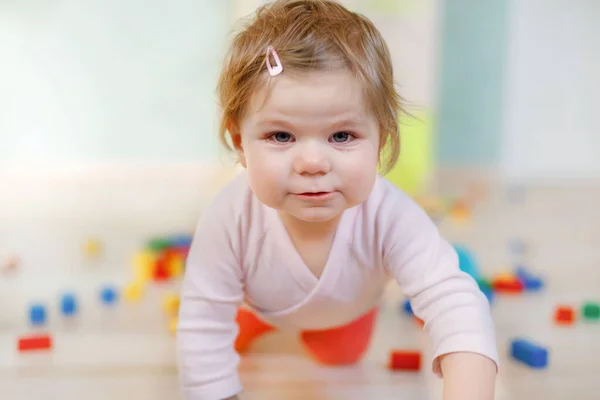 Eğitici oyuncaklarla oynayan tatlı küçük bir kız. Mutlu sağlıklı çocuk evde ya da çocuk odasında renkli tahta bloklarla eğleniyor. Bebek sürünüyor, renkleri ve biçimleri öğreniyor. — Stok fotoğraf