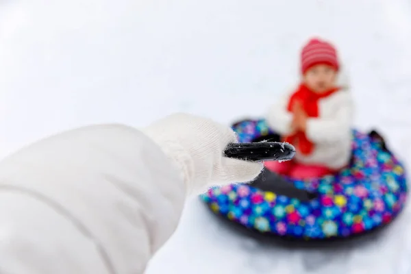 妈妈把小女孩拉到雪筒上。可爱的小快乐的孩子在冬天穿着五彩缤纷的轮胎在户外玩.家庭、女儿和妇女在雪地的森林里徒步旅行和散步，户外. — 图库照片